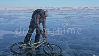 人和他的自行车在冰上。 骑自行车的人穿着灰色的<strong>羽绒服</strong>，背包和头盔。 冰冻湖的冰